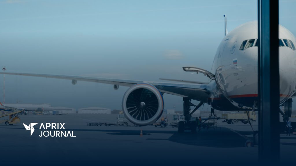 A imagem mostra a visão de frente da turbina de um avião, por trás da janela de um aeroporto