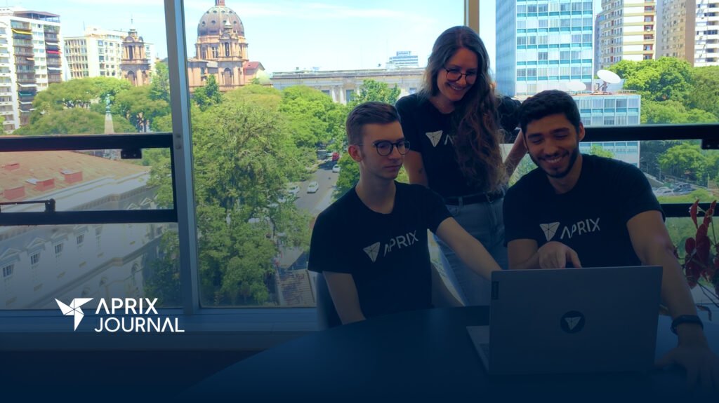 Três pessoas vestem a camiseta da Aprix enquanto trabalham olhando para um notebook.
